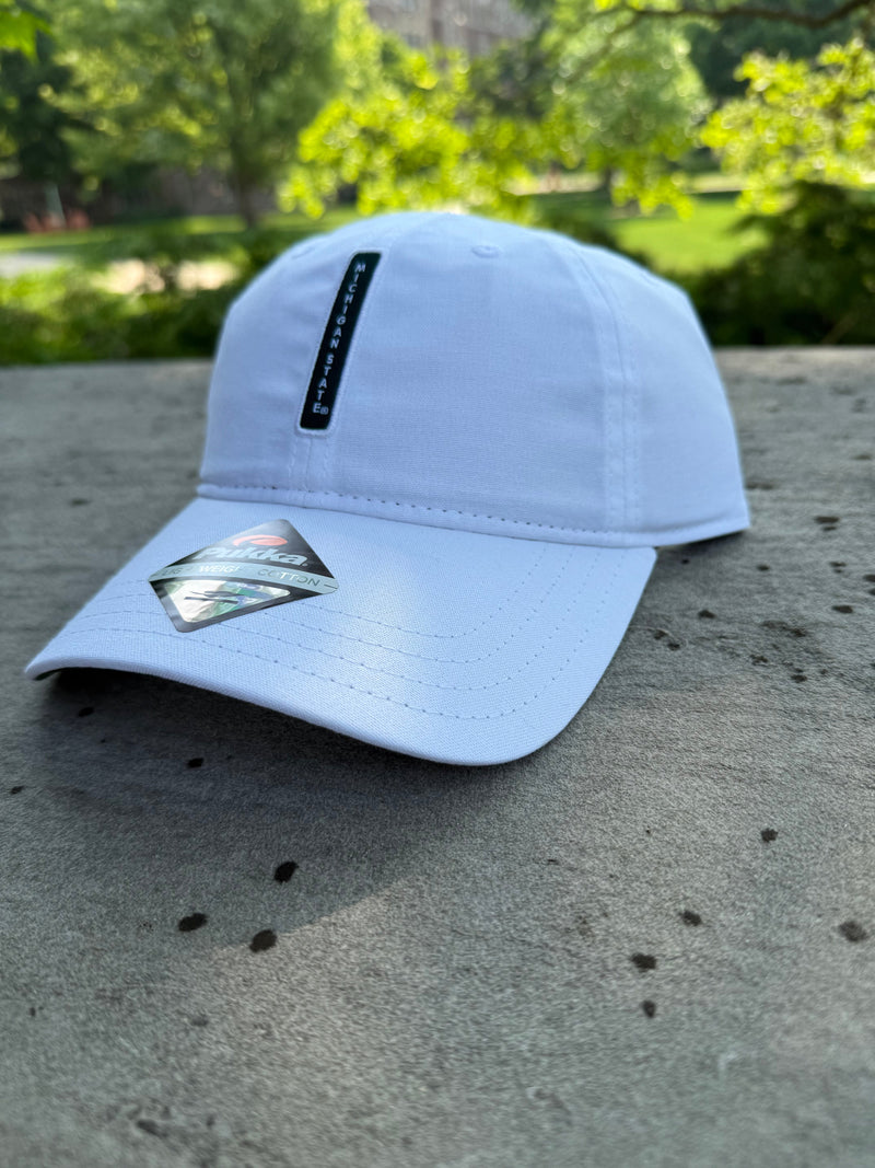 White cap with a curved bill leaning on a concrete wall outside. Green vertical bar in the center that reads Michigan State.
