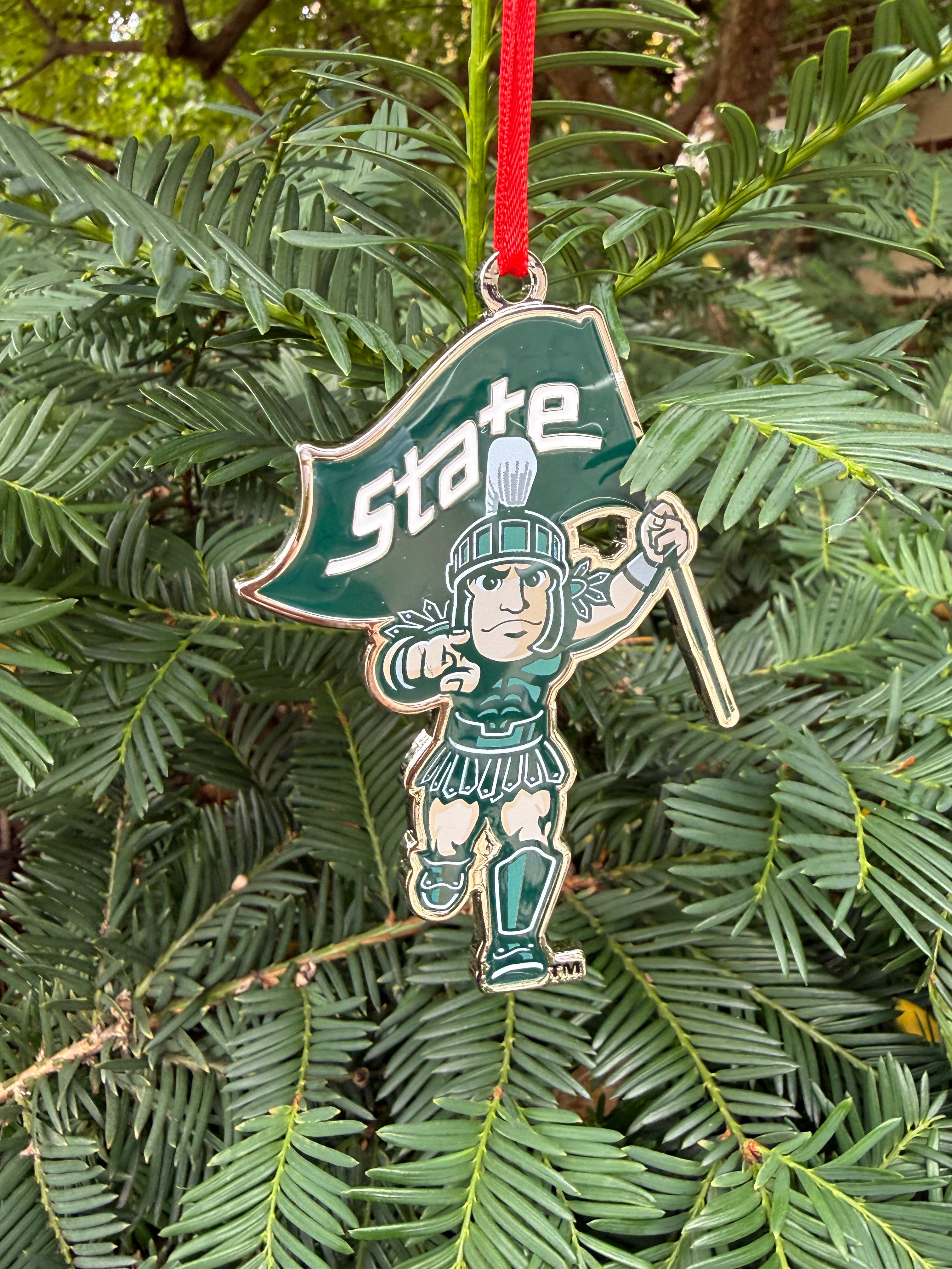 Decorative running Sparty ornament. Sparty is in a running formation while holding a green flag with a bold 'State' wordmark on it. 