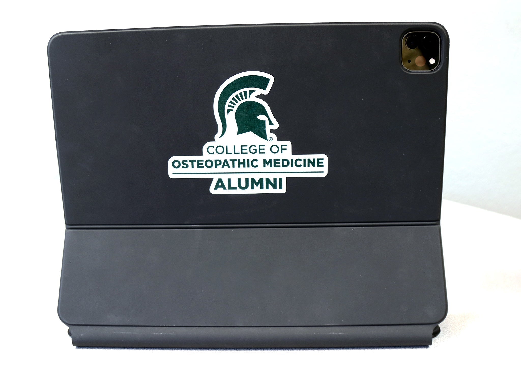 Back of black laptop with a white decal with the Spartan helmet and College of Osteopathic Medicine Alumni in forest green. 