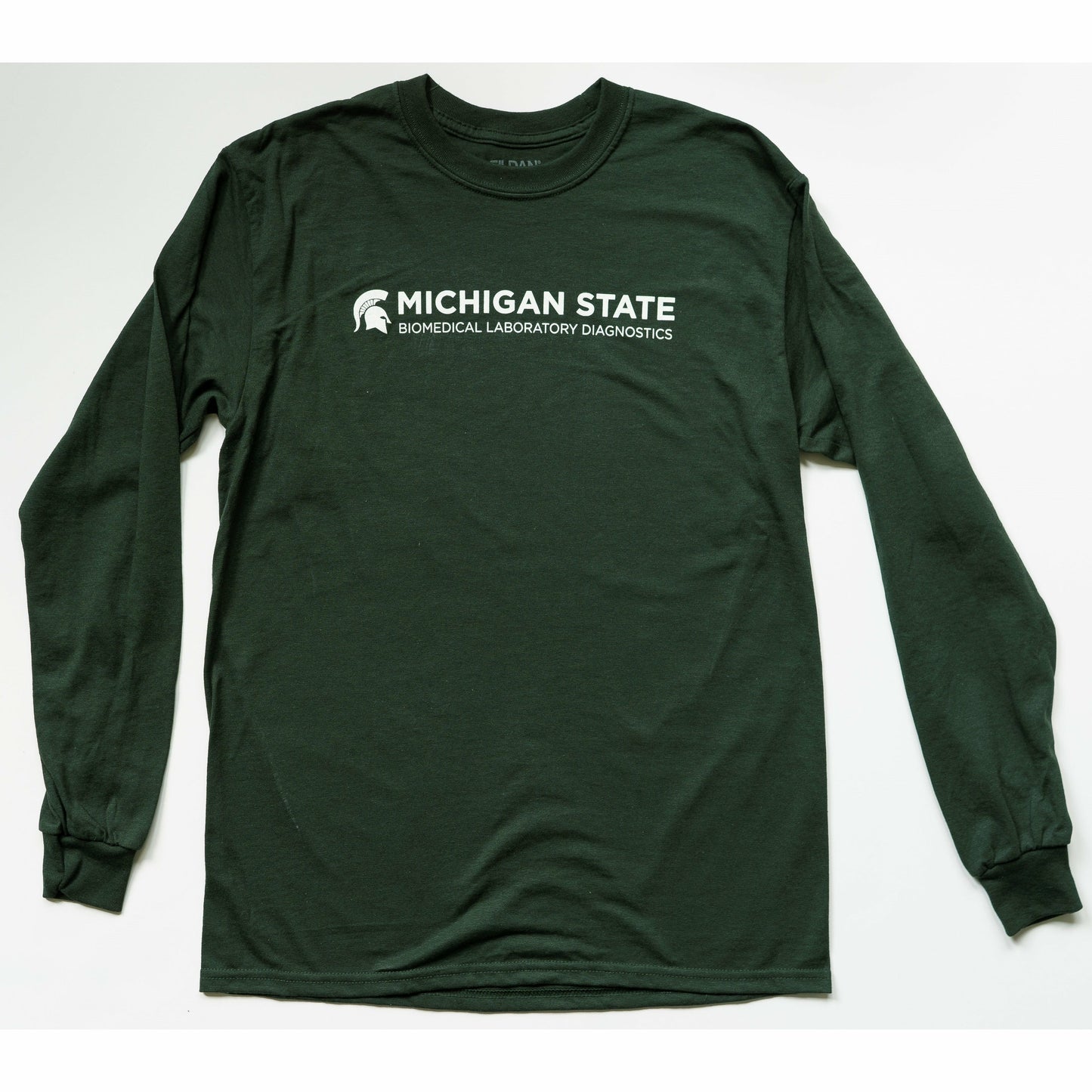 Forest green crewneck T-shirt with long sleeves. Across the center chest is text on two lines reading "Michigan State" (in bold) and "Biomedical Laboratory Diagnostics." To the left of the text is a white Spartan Helmet.