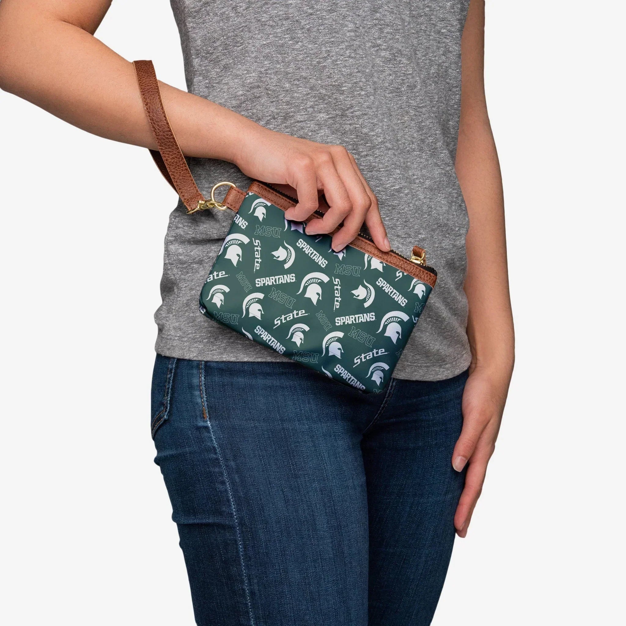 Person holding small rectangular green wristlet with white printed Spartans, State, and MSU work marks as well as white Spartan helmets all over design. Brown faux leather trim and wristlet loop. Zipper closure. 