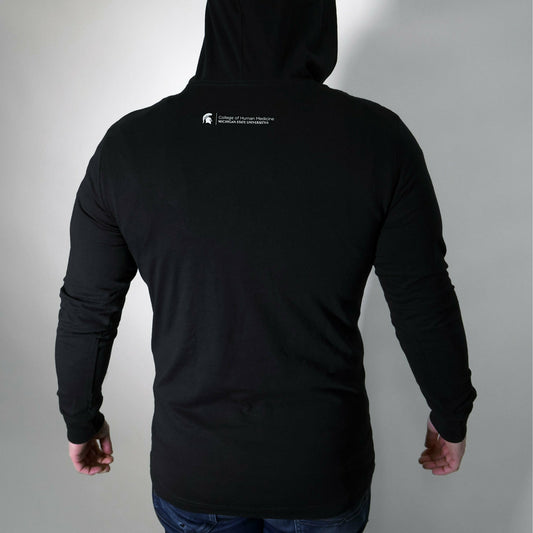 Back of a man wearing the black long-sleeve T-shirt with the hood up. Under the hood is the College of Human Medicine signature logo.