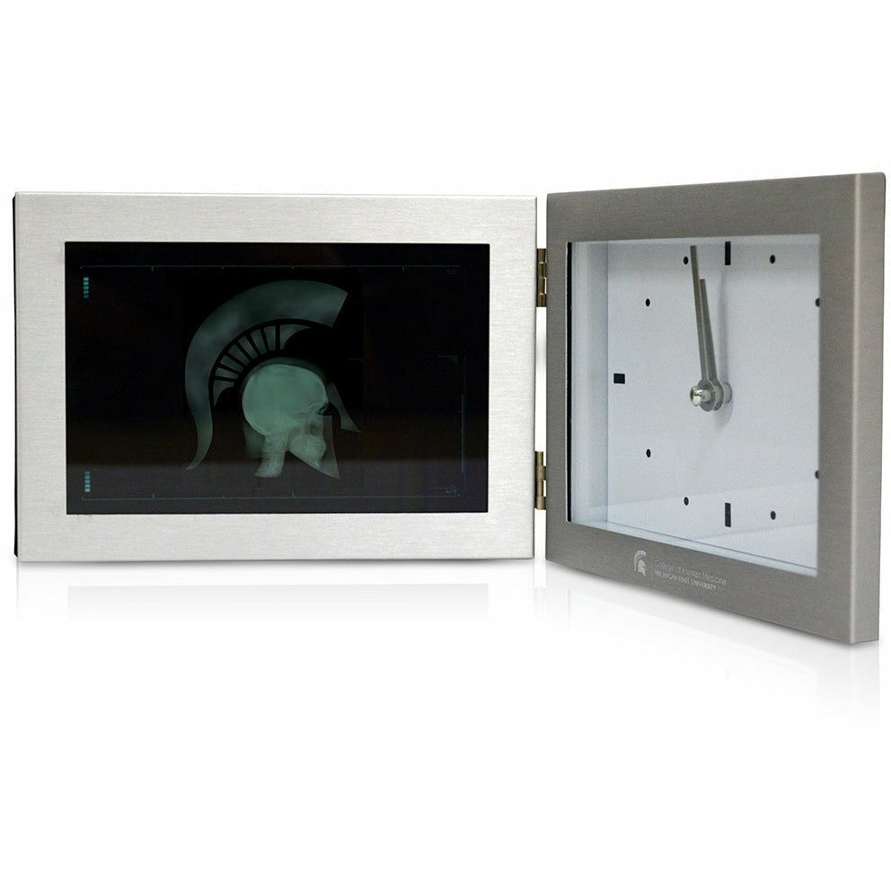 Silver foldable clock. On one side is a framed photo of the MD Sparty graphic (an x-ray of a head wearing a Spartan Helmet). The other side features a modern clock face above an engraved College of Human Medicine signature logo