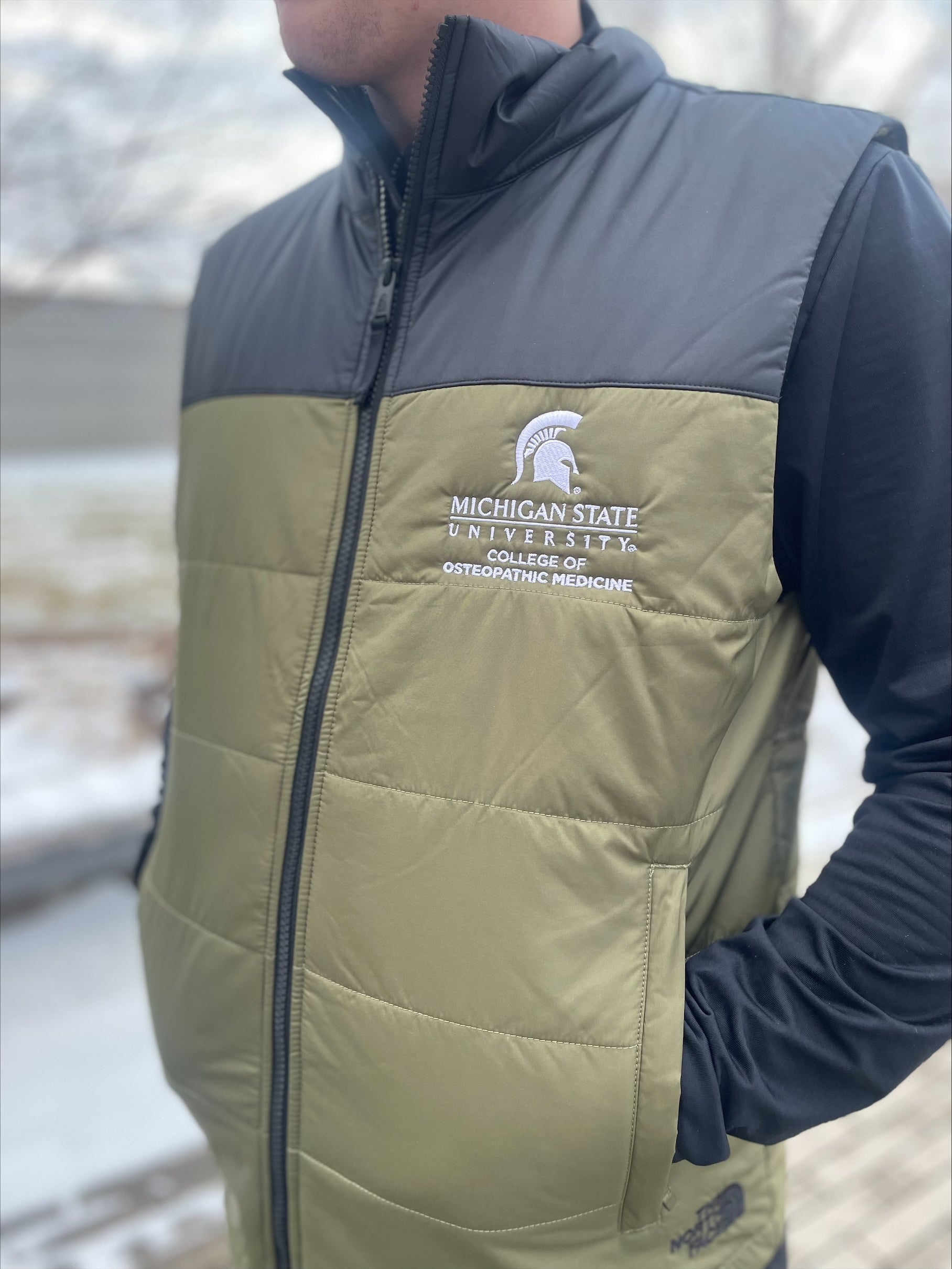 Close up of a green and black vest with a white embroidered Michigan State University College of Osteopathic Medicine logo on the left chest. 