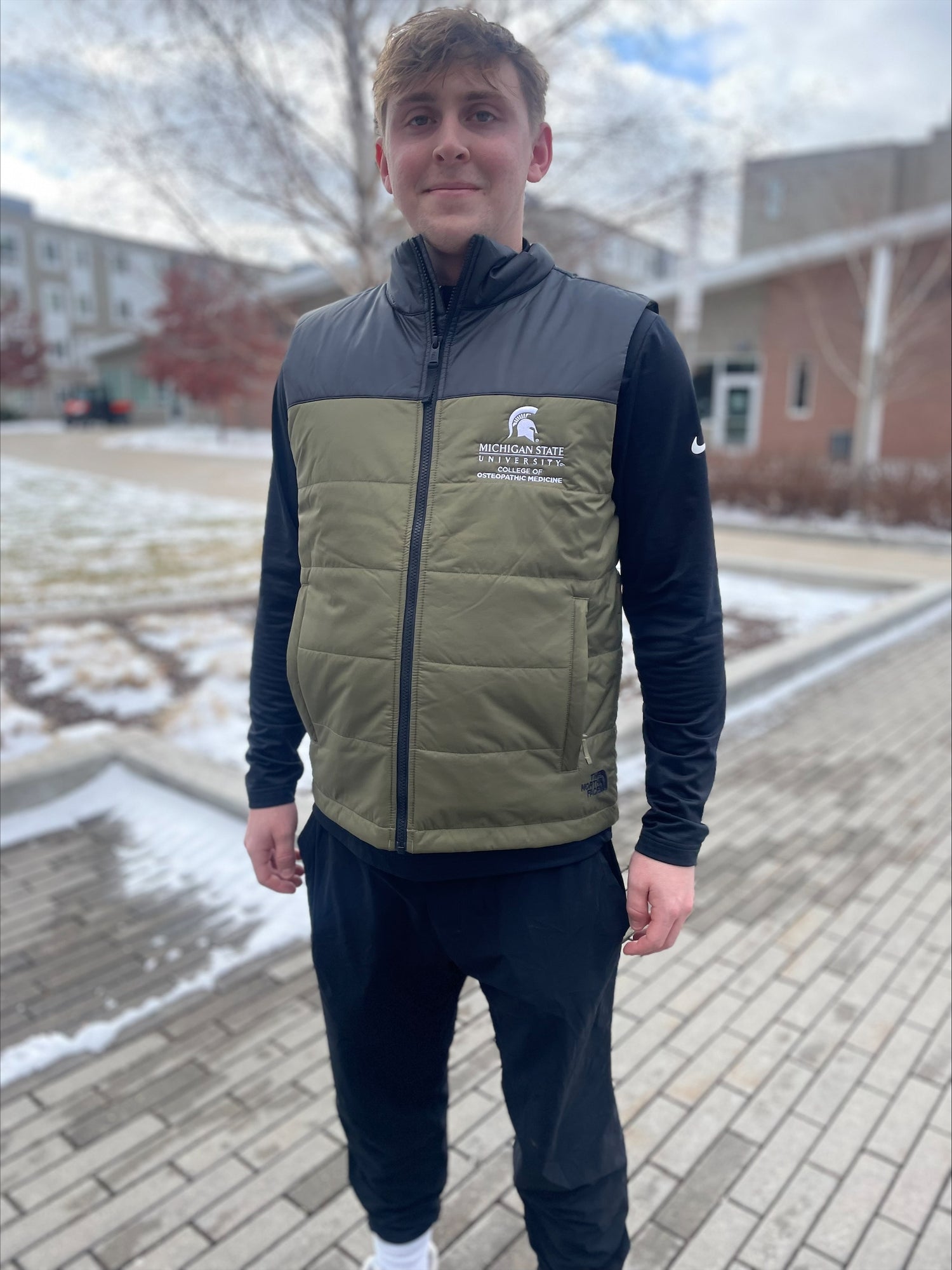 Person wearing a green and black vest with a white embroidered Michigan State University College of Osteopathic Medicine logo on the left chest. 