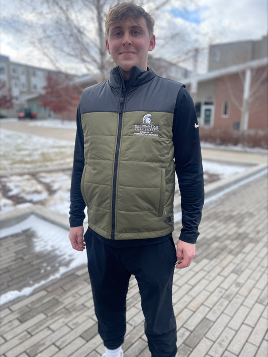 Person wearing a green and black vest with a white embroidered Michigan State University College of Osteopathic Medicine logo on the left chest. 