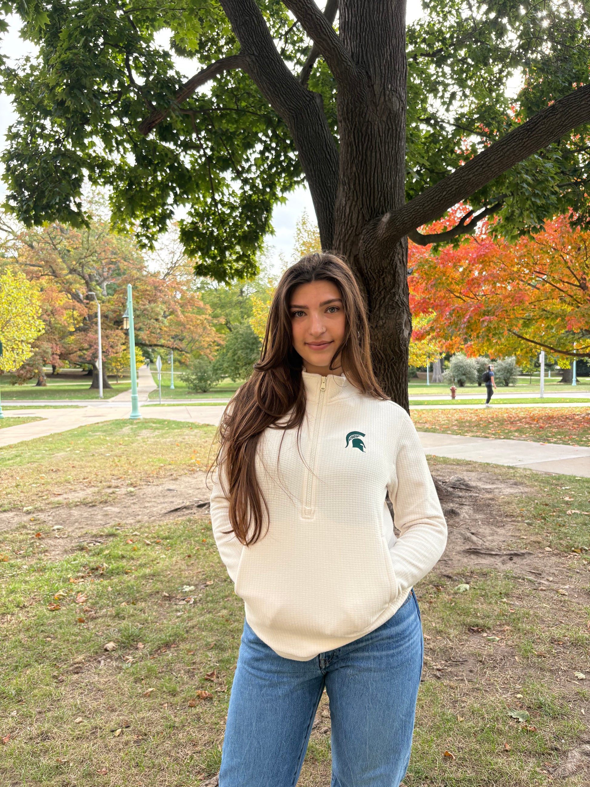 Women standing outdoors, wearing a off white waffle knit half zip pullover with a green embroidered Spartan helmet logo on left chest.