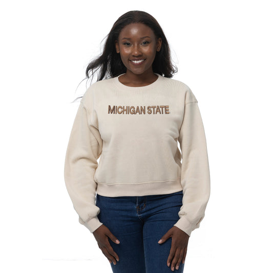 Woman wearing a cropped beige crewneck sweatshirt with a brown "Michigan State" wordmark on the front. Shown on a white background.