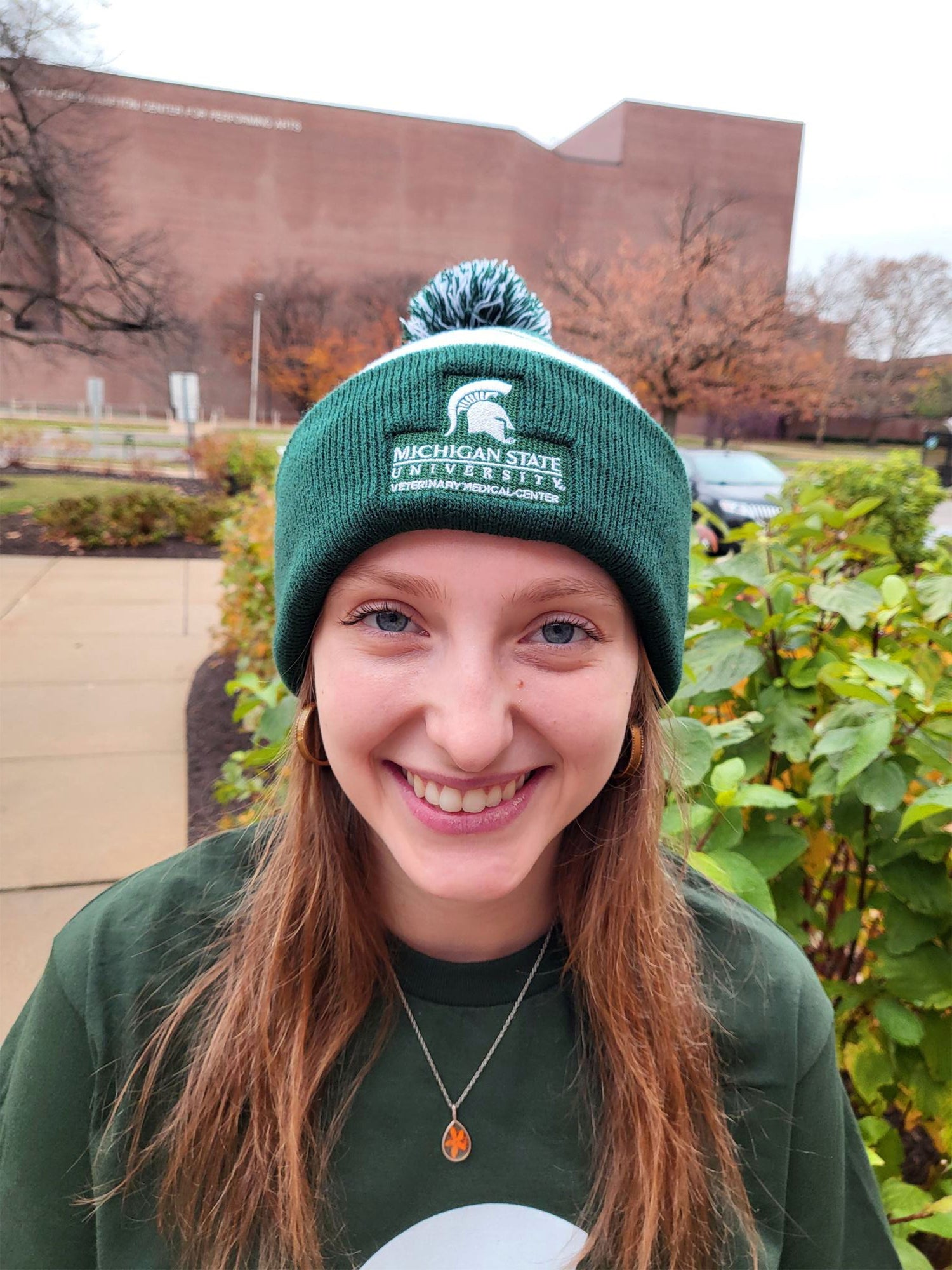 A woman wearing a green and white striped beanie. The beanie is embroidered with a white Spartan helmet logo and Michigan State University Veterinary Medical Center logo.