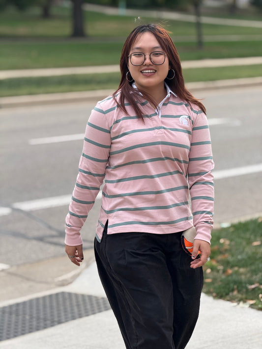Person wearing a pink and soft green striped long-sleeved shirt with a white embroidered Spartan logo on the left upper chest and a white collar and button down placard. 