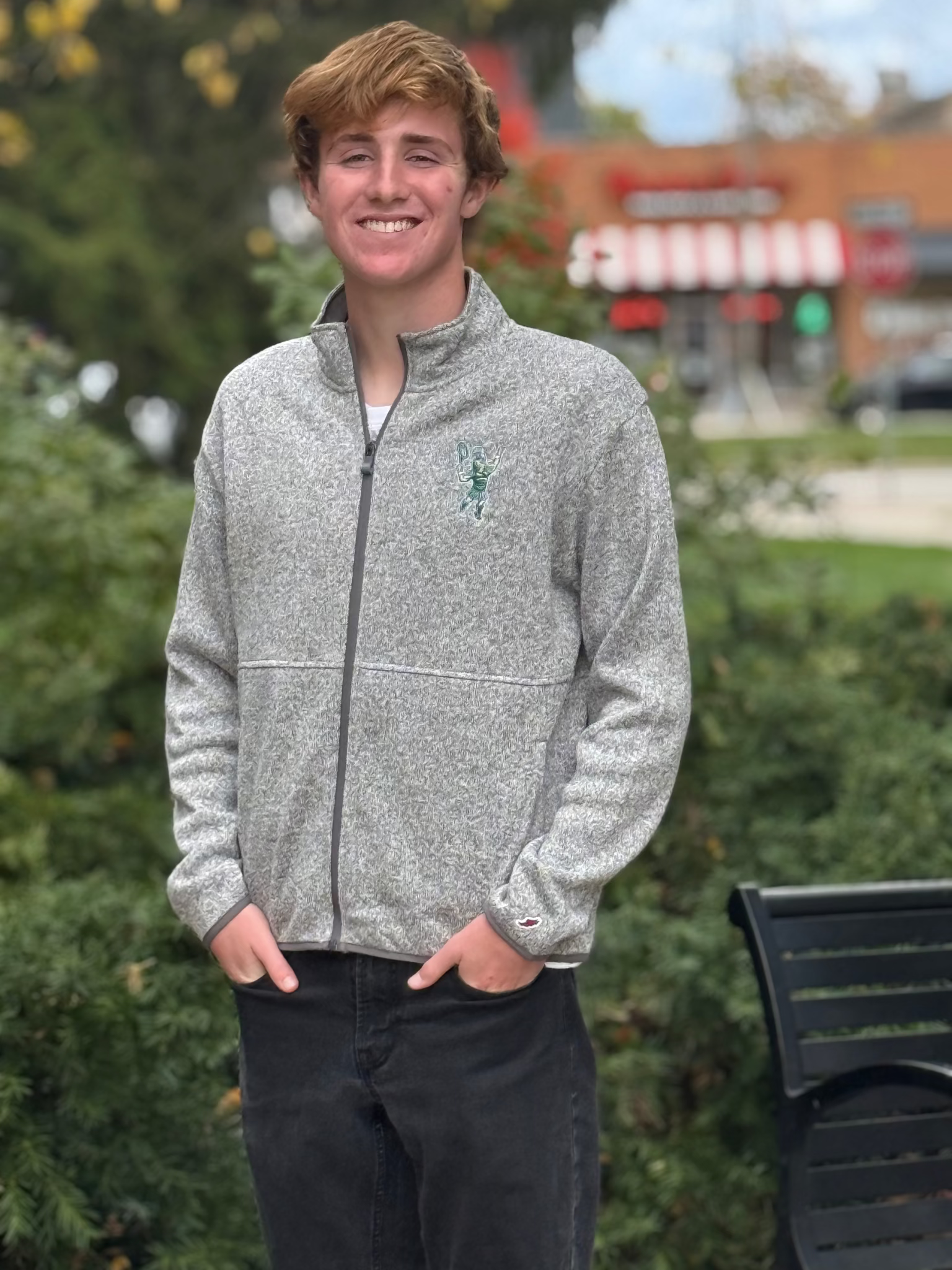 Full-zip mock neck heathered gray jacket with darker gray sleeve hems and zipper. On the left upper chest there this is an embroidered Sparty playing tennis. 