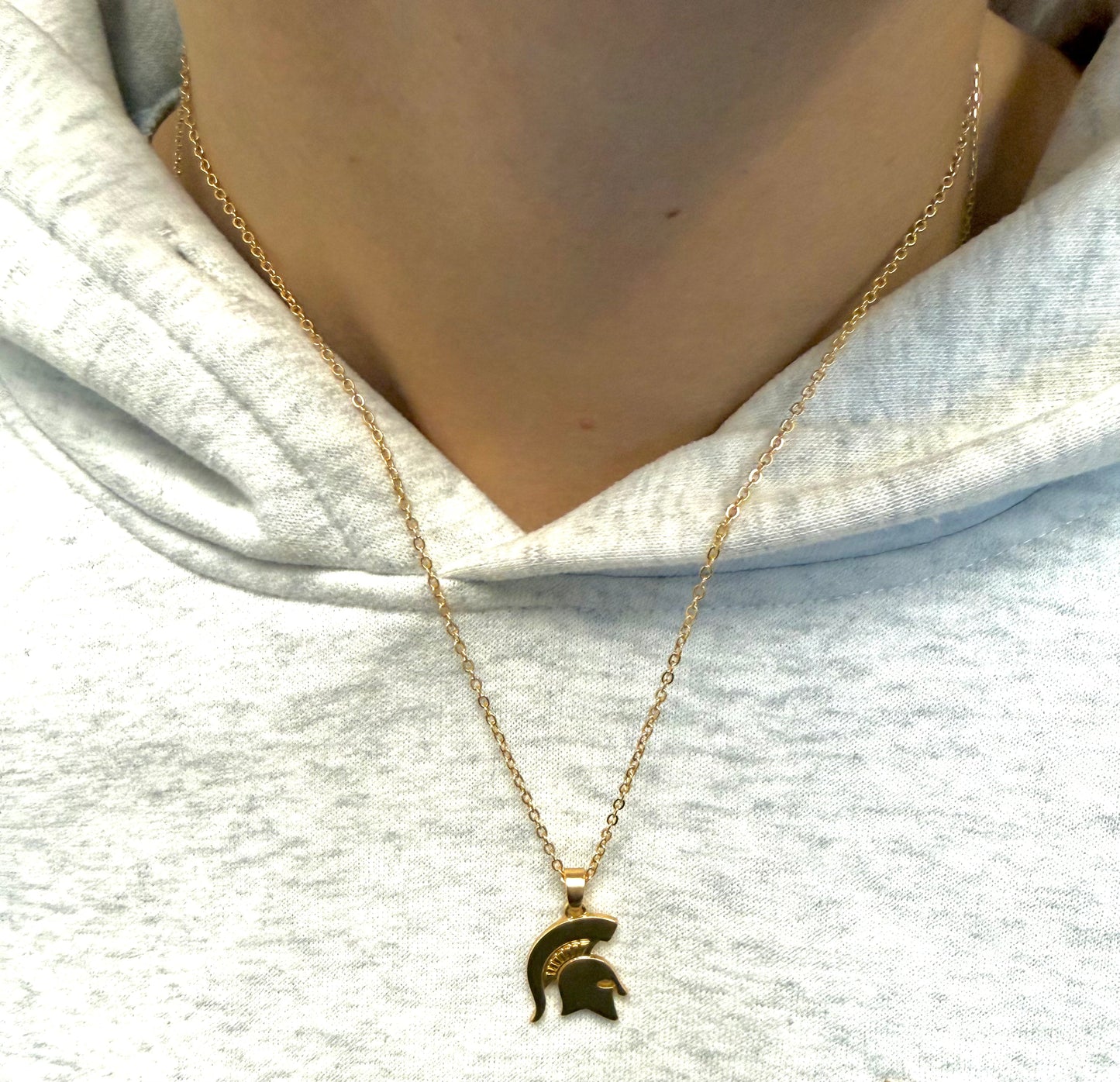 Close up of a person wearing a gold chain link necklace with a gold Spartan Helmet pendant.