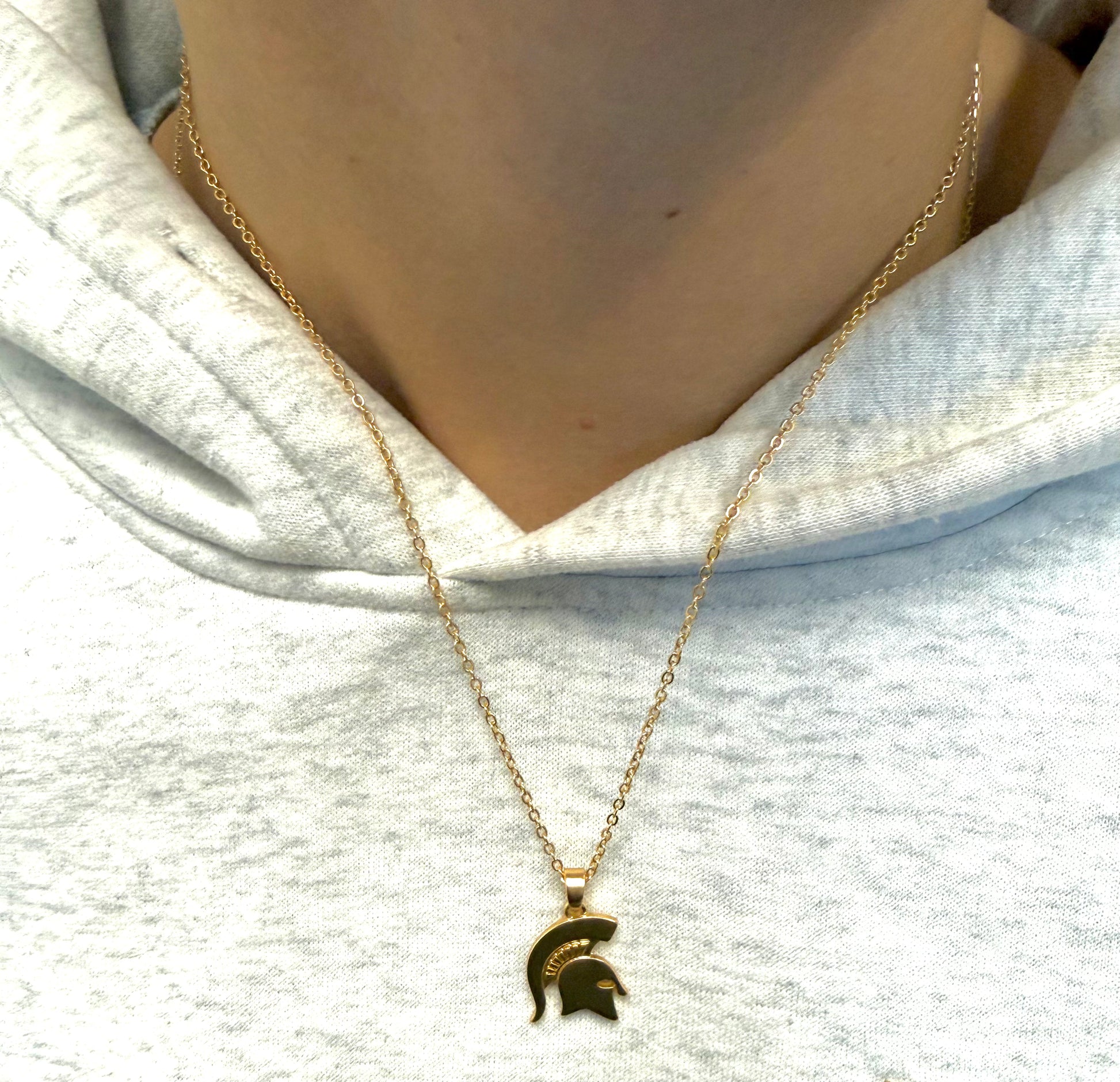 Close up of a person wearing a gold chain link necklace with a gold Spartan Helmet pendant.