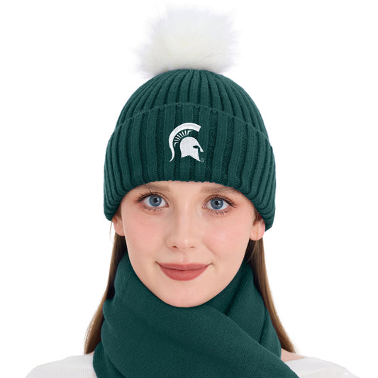 Close-up view of a model wearing a dark green rib-knit Michigan State Spartans beanie featuring an embroidered white Spartan helmet logo on the front and a large white faux-fur pom-pom on top. The beanie is paired with a matching dark green scarf wrapped around the neck.