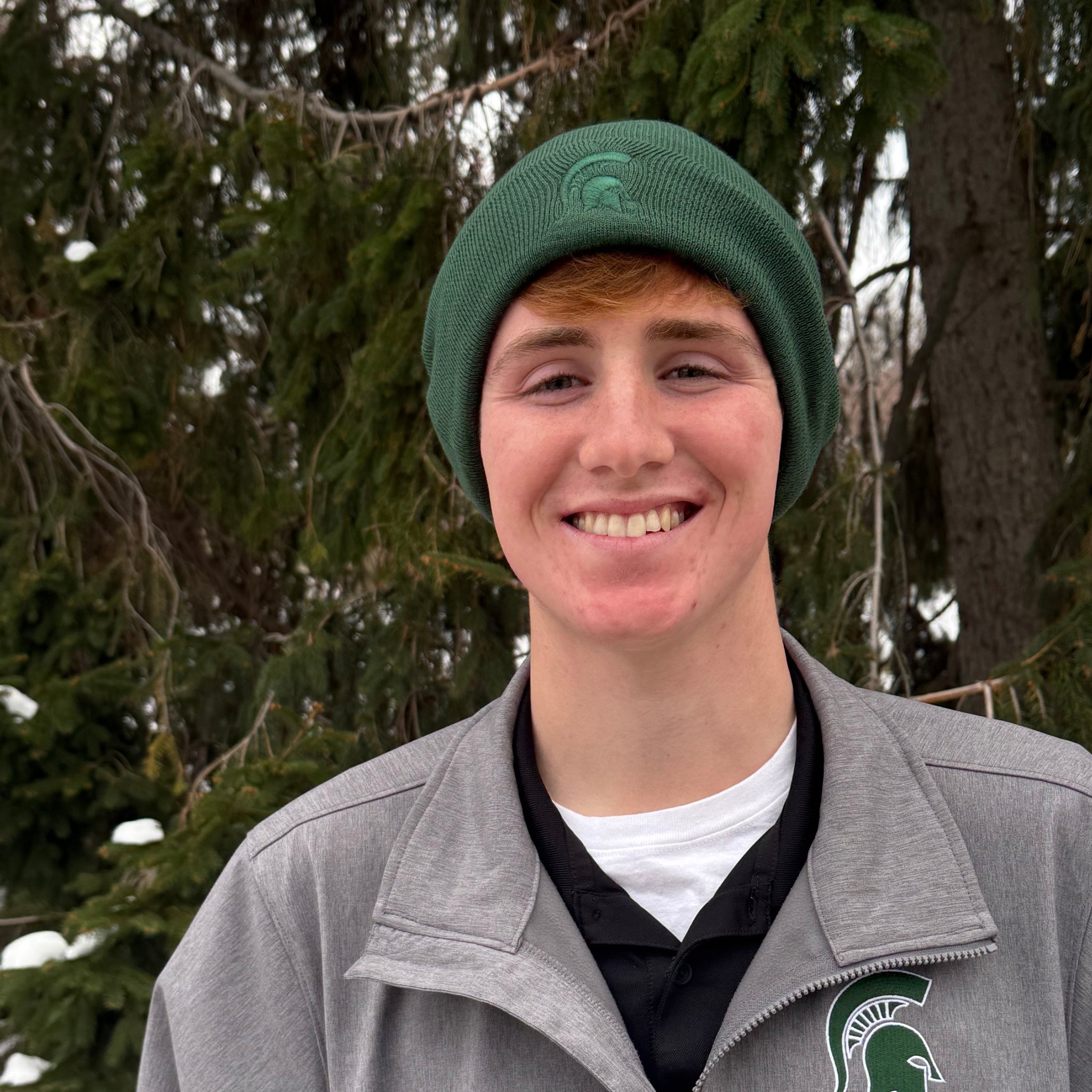 Person wearing green cuffed knit beanie. Center on cuff is a green Spartan Helmet logo that is embroidered. 