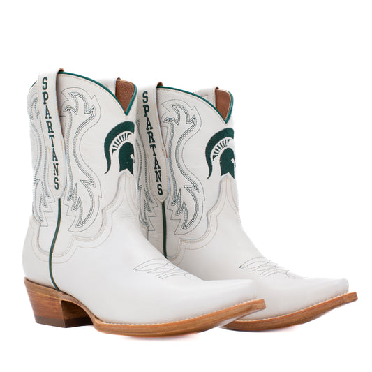 A pair of white leather cowboy boots featuring the Michigan State Spartans logo and 'SPARTANS' text on the shaft, with green and gray detailing and brown stacked heels.