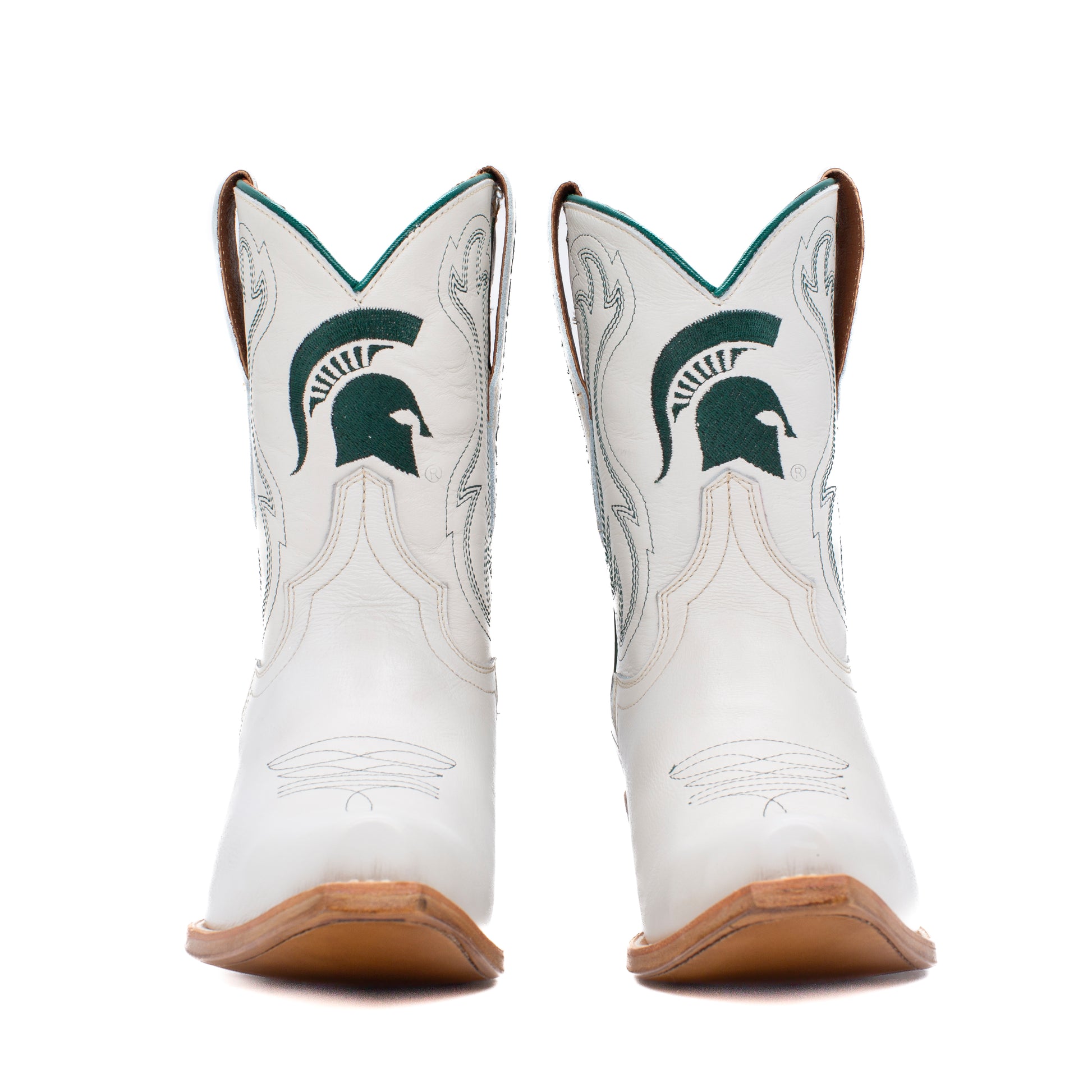 A pair of white western cowboy boots featuring the Michigan State Spartans logo in dark green on the shafts, with light gray decorative stitching and tan soles. 