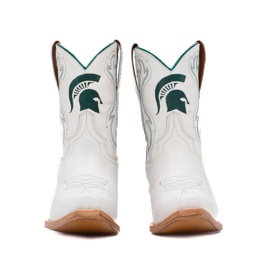 A pair of white western cowboy boots featuring the Michigan State Spartans logo in dark green on the shafts, with light gray decorative stitching and tan soles. 