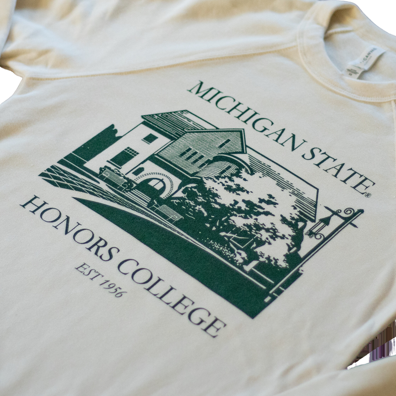 A natural/tan colored crewneck sweatshirt. On the torso of the sweatshirt in green is an image of the first MSU honors college building. Around the image is the text "Michigan State Honors College est. 1956."