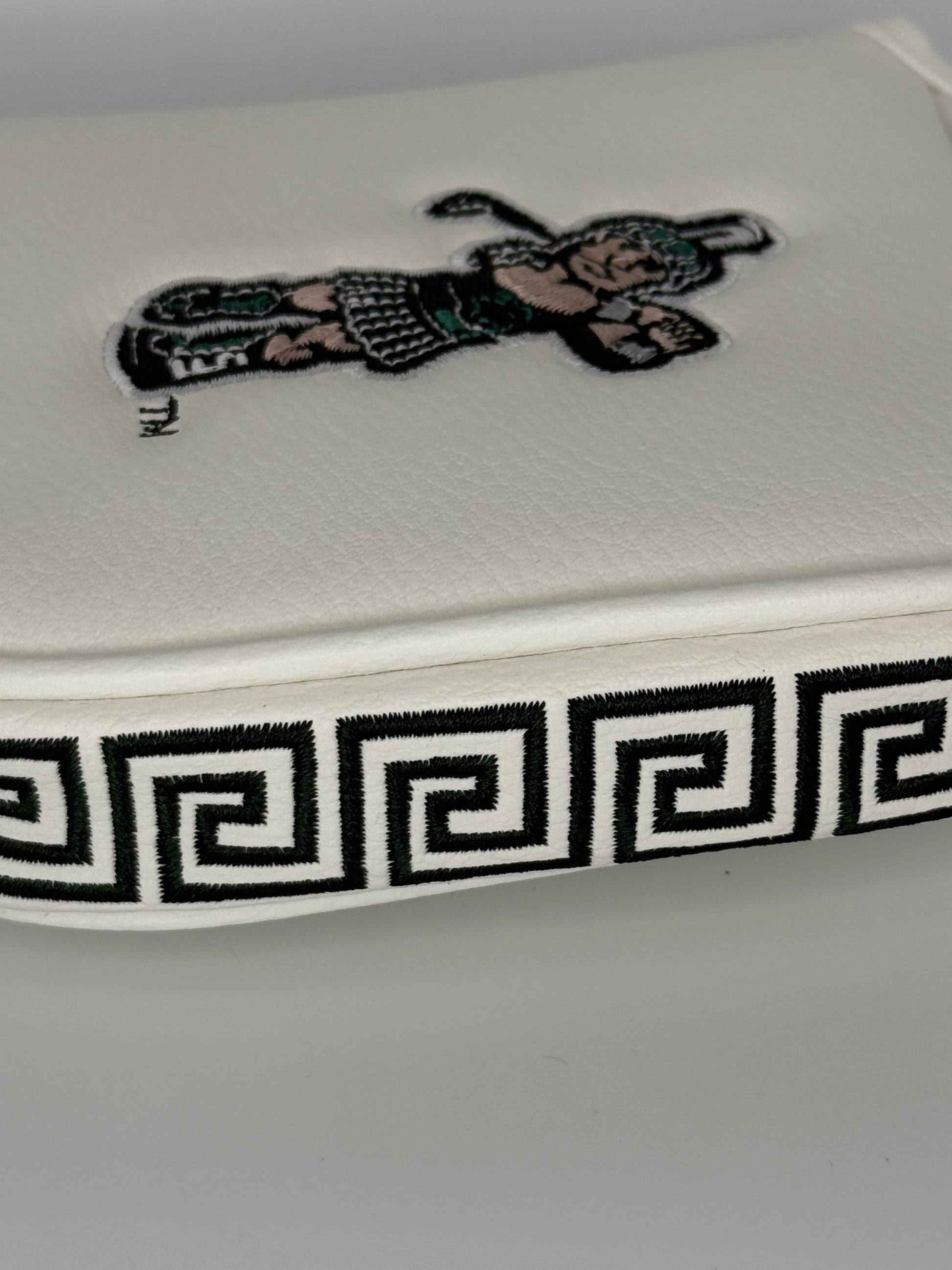 Close up of a white mallet putter headcover with an embroidered Golf Sparty logo on the front and a green and white Greek design on the side. 