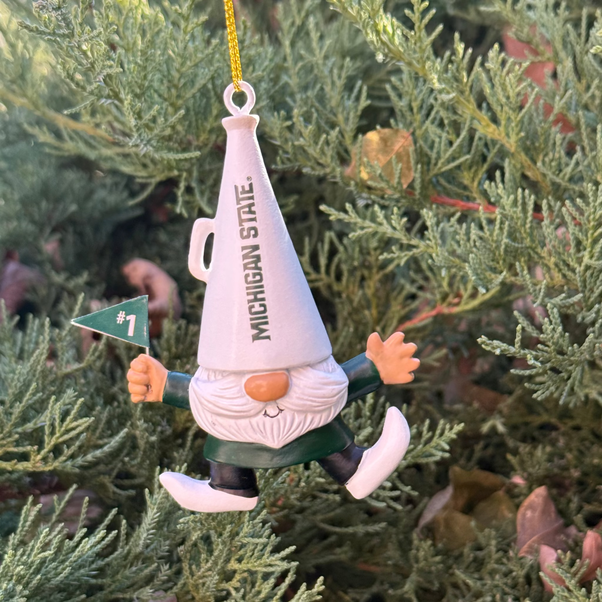 Gnome ornament with a white megaphone over its head that has "Michigan State" written vertically in green on it. The Gnome is wearing a green shirt, black pants, and white shoes whilst holding a green flag with the number one on it. 