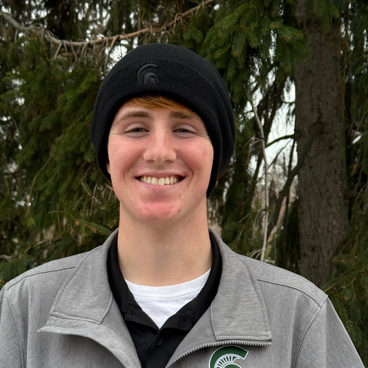 Person wearing a black cuffed knit beanie with a black embroidered Spartan Helmet logo centered on cuff. 