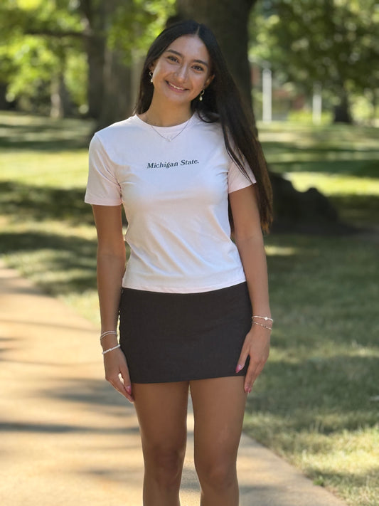 Person wearing a light pink slim fit short sleeve top. Screen printed in a small to medium print is Michigan State in green. 