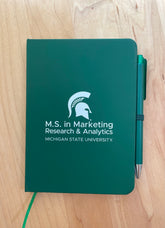 Green notebook with the M.S. in Marketing Research & Analytics Michigan State University logo printed in white. 