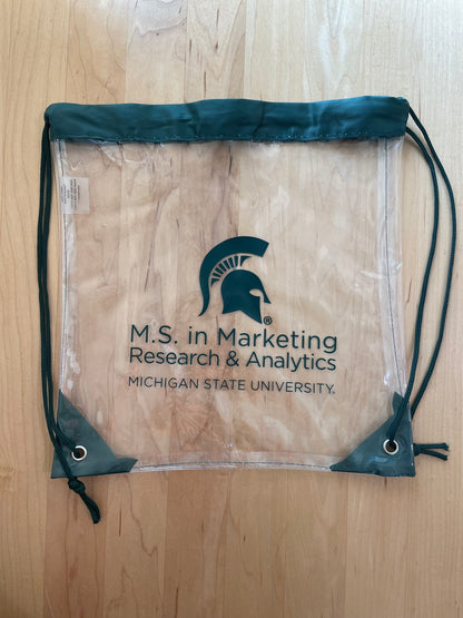 Clear drawstring backpack with the M.S. in Marketing Research & Analytics Michigan State University logo printed in green. Green trim and string handles. 
