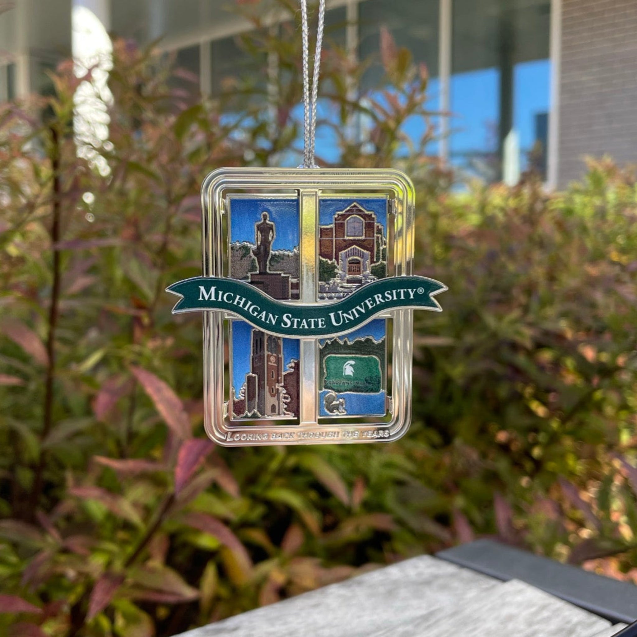 Collectable ornament. Michigan State University emblem on a green banner and various campus icons with a "Looking back through the years" wordmark at the bottom of the ornament.
