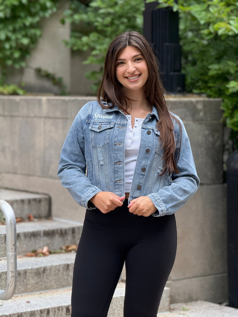 Woman wearing a denim jacket standing outdoors on steps with greenery in the background