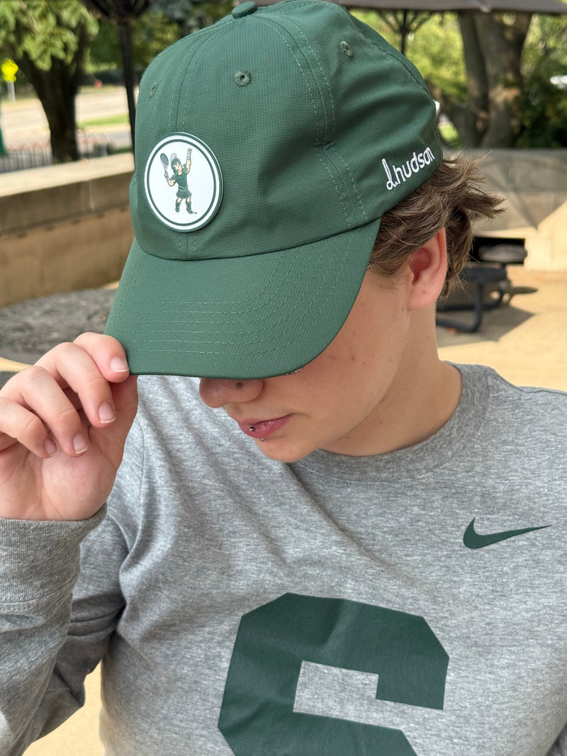 Person wearing a green cap with a Tennis Sparty logo, standing outdoors.