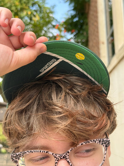 Person holding a green cap with a tennis court design underneath the bill.