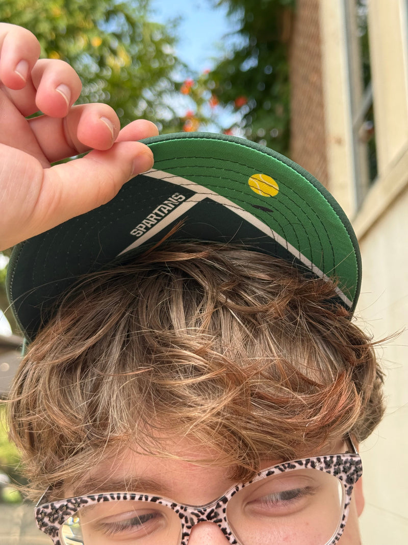 Person holding a green cap with a tennis court design