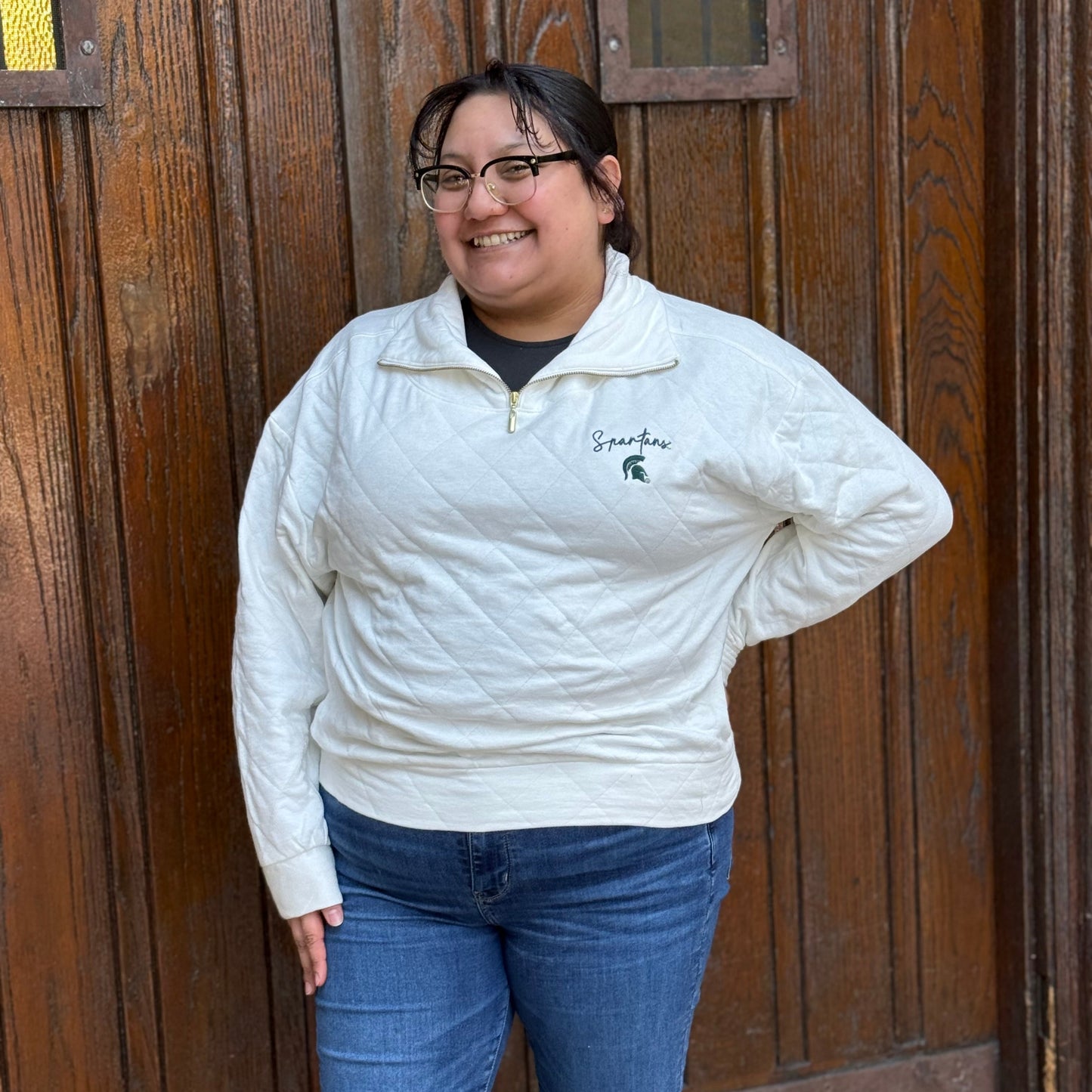 Woman wearing a cream quarter-zip with a gold zipper, "Spartans" written in green script text, and the Spartan Helmet logo embroidered underneath in green.
