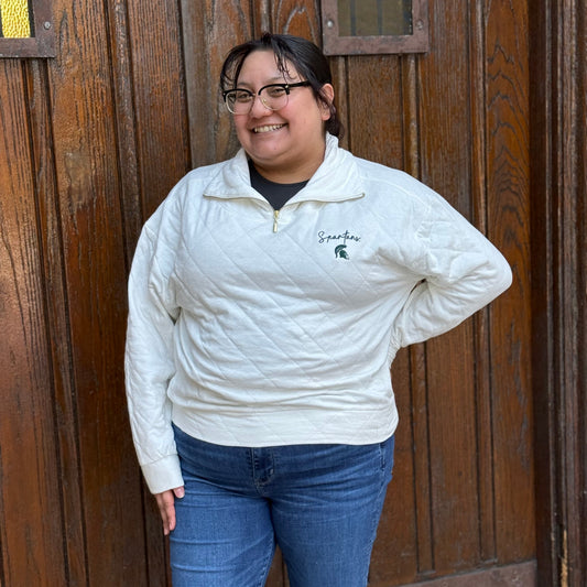 Woman wearing a cream quarter-zip with a gold zipper, "Spartans" written in green script text, and the Spartan Helmet logo embroidered underneath in green.