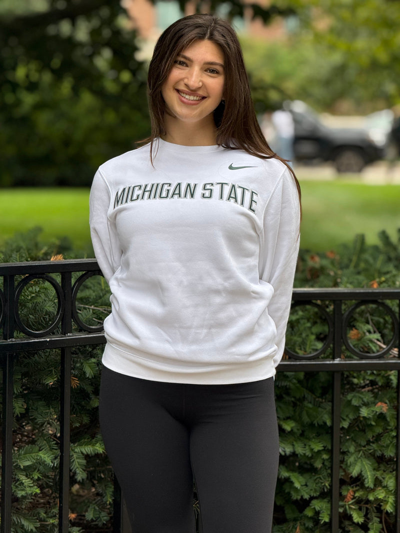 Woman wearing a Michigan State sweatshirt standing outdoors with greenery in the background
