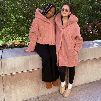 Two woman modeling the Jill Martin pink loungers. The woman on the left of the image is sitting, wearing the cropped pink lounger with a hood. The woman on the left is standing, wearing the long pink lounger with her hand in the pocket. 