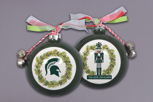 Two festive Christmas ornaments with red and white striped strings and silver bells. One features a green Spartan helmet surrounded by a holly wreath, and the other shows a nutcracker in green attire with a holly wreath and 'TIS OUR SEASON' text. Both are decorated with red, green, and white ribbon bows.