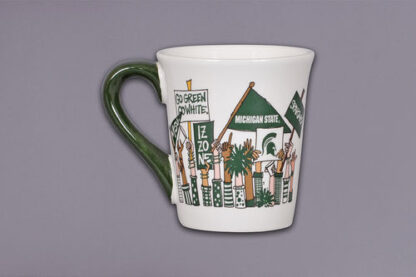 White ceramic mug with green handle featuring illustrations of people holding Michigan State University-themed signs and banners, including text such as 'GO GREEN GO WHITE,' 'IZZONE,' and 'MICHIGAN STATE.