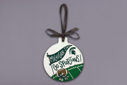 Round ornament with a black ribbon, featuring a green and white design with 'MICHIGAN STATE' on a flag, 'GO SPARTANS!' text, a football, flowers, and part of a football field