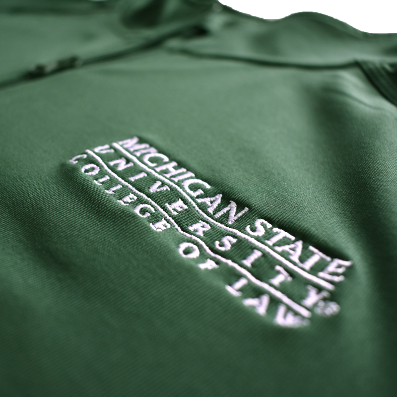 Close-up of the embroidered white Michigan State University College of Law wordmark logo on the left chest of a dark kelly green jacket.