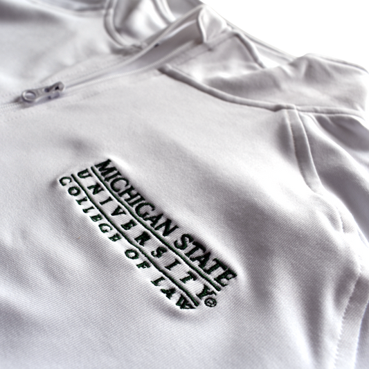 Close-up of the embroidered forest green Michigan State University College of Law wordmark logo on the left chest of a white jacket.