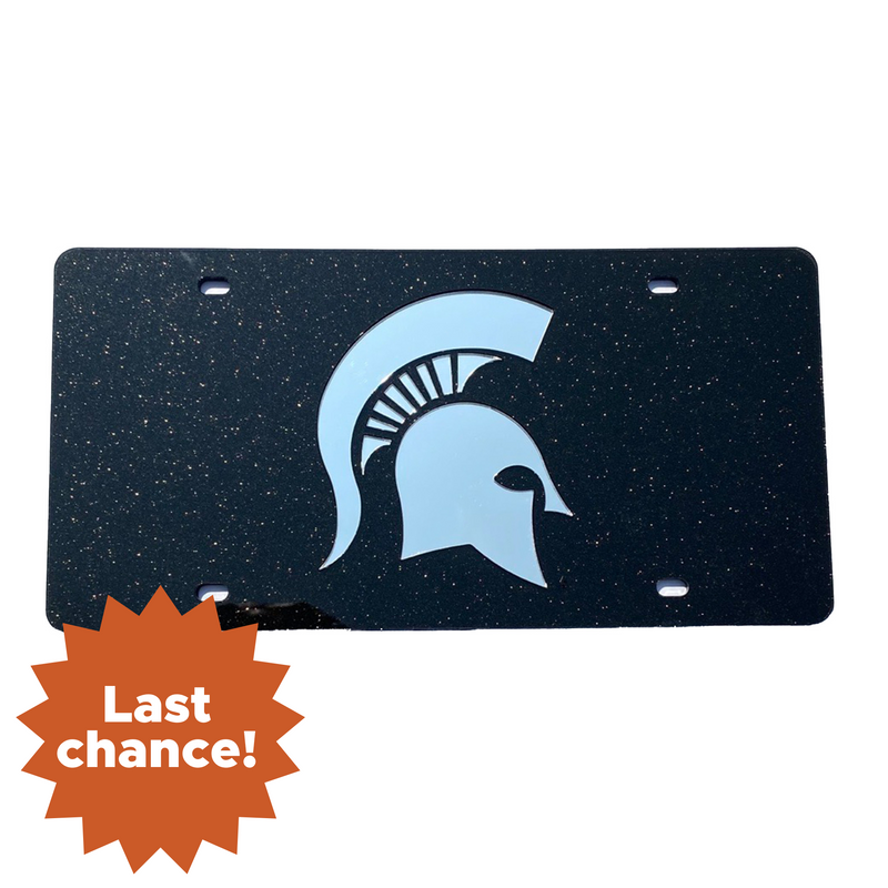 Black license plate featuring a white Spartan helmet logo in the center, with four mounting holes—one in each corner. An orange starburst in the bottom left corner reads 'Last chance!