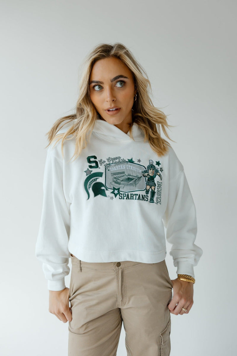 Person wearing a white hoodie featuring green graphics including the letter "S", a Spartan helmet, the word "SPARTANS", a Spartan figure illustration, and decorative stars.