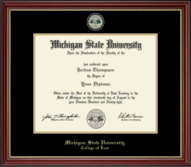 The diploma is enclosed in a dark wood frame with a black matte with gold accents and gold trim. In gold cursive letters 'Michigan State University' at bottom. Below in gold cursive letters 'College of Law'. Top of matting is gold engraved Michigan State University seal. 