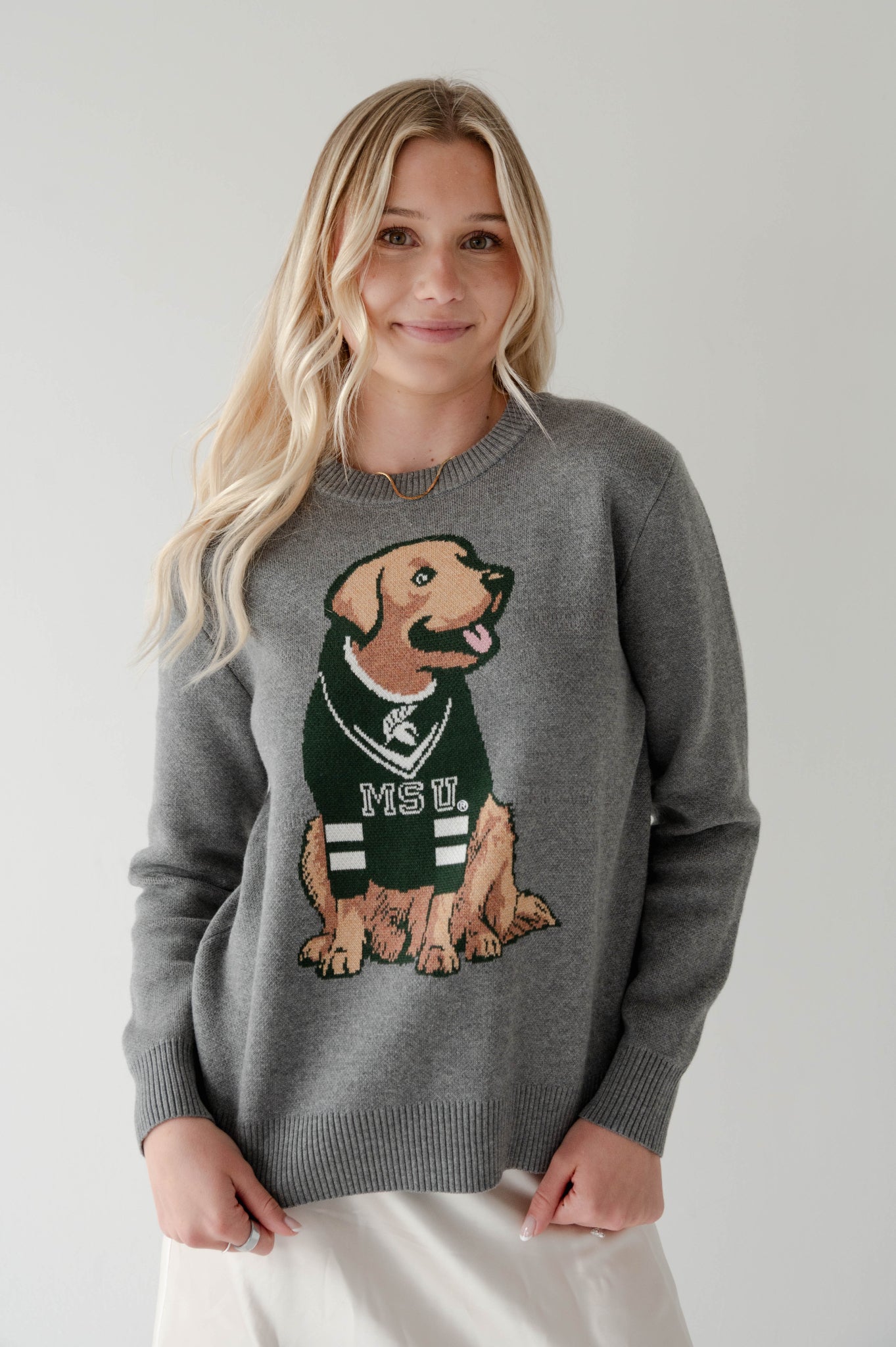 Young woman wearing a gray Michigan State University sweater featuring a large dog graphic in a green MSU jersey.