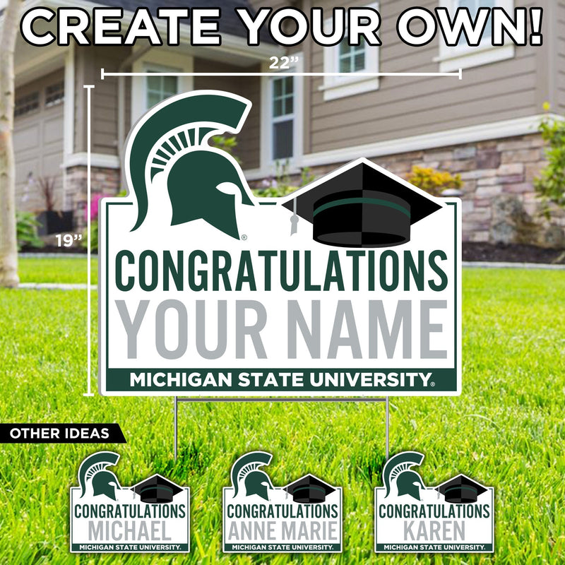A white customizable yard sign with 'CONGRATULATIONS' text in green, a black graduation cap, and a Michigan State Spartan helmet in green at the top. At the bottom is a green stripe with the words 'Michigan State University' in white.
