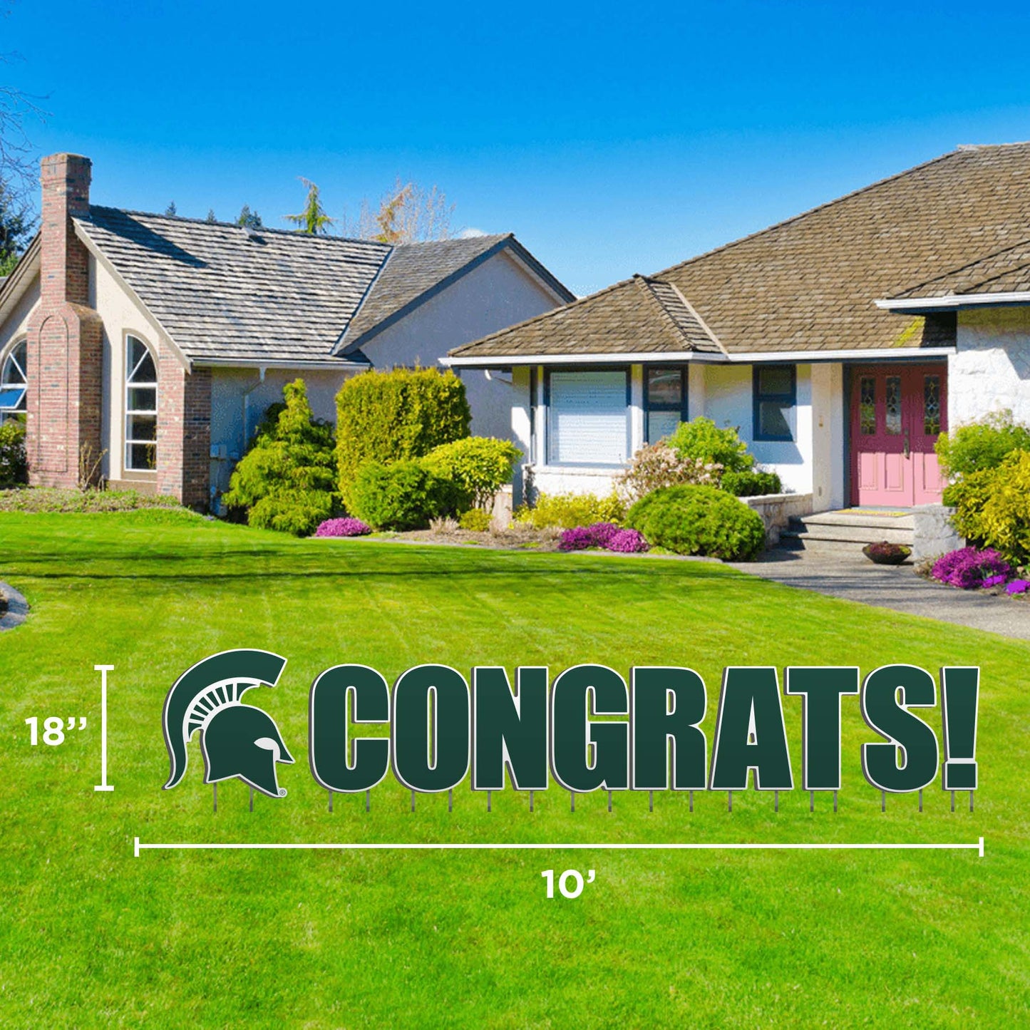 A lawn display featuring the text 'CONGRATS!' with the Michigan State University Spartan helmet logo in green outlined in white, set against a backdrop of a residential area.