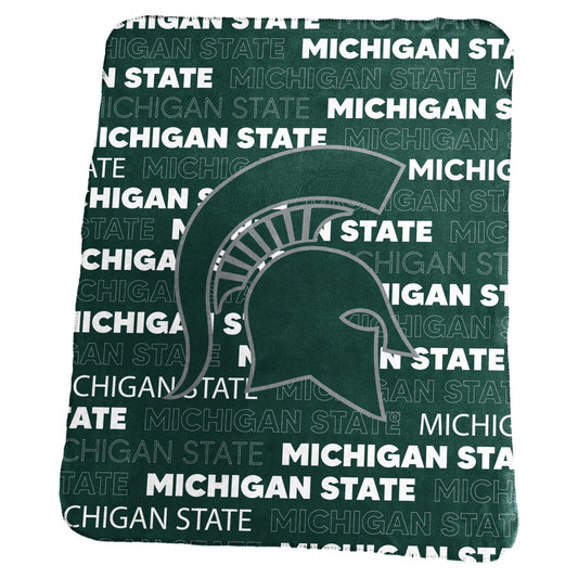 Green and white blanket with the words Michigan State repeated in various fonts. Center of blanket is a large green Spartan helmet outlined in grey. 